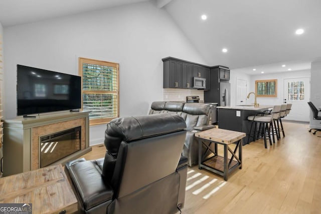 living area with light wood-type flooring, recessed lighting, beam ceiling, and a glass covered fireplace