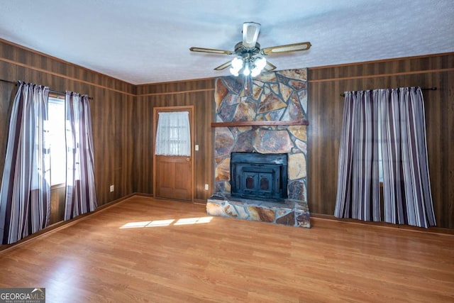 unfurnished living room featuring a ceiling fan, wood finished floors, a wood stove, a textured ceiling, and wood walls