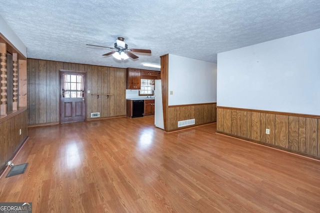 unfurnished living room with a wainscoted wall, a textured ceiling, wood finished floors, and visible vents