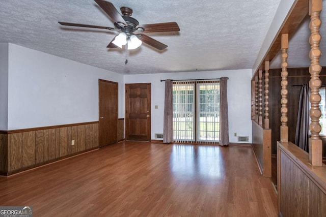 interior space featuring wainscoting, visible vents, a textured ceiling, and wood finished floors