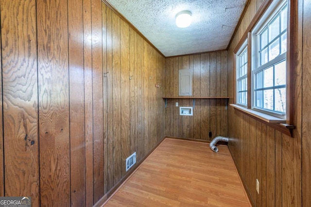 laundry area featuring a textured ceiling, laundry area, light wood-style flooring, and wooden walls