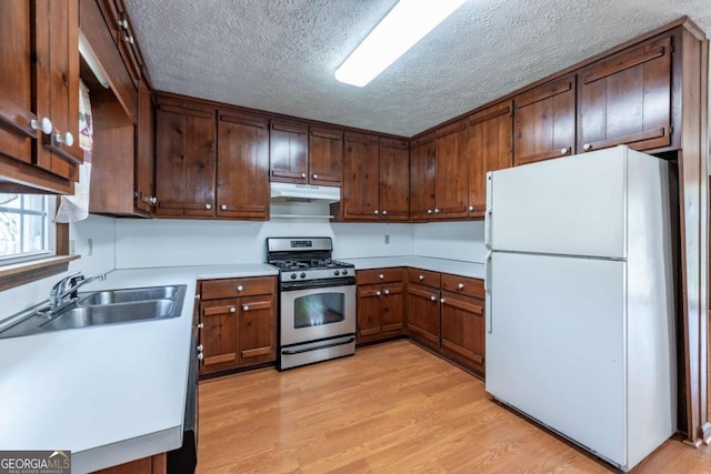 kitchen with under cabinet range hood, a sink, light wood-style floors, freestanding refrigerator, and gas stove