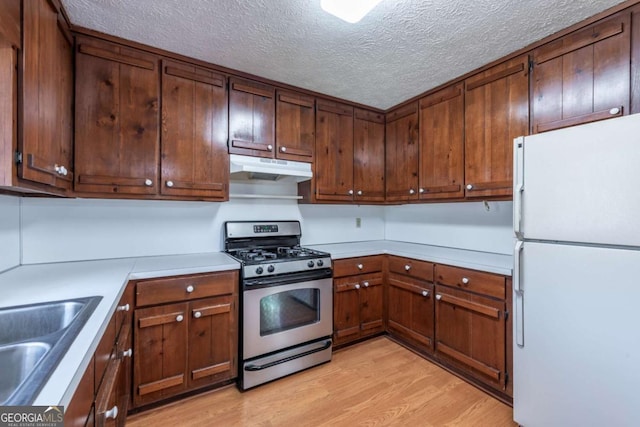 kitchen featuring stainless steel gas range, under cabinet range hood, light wood finished floors, and freestanding refrigerator