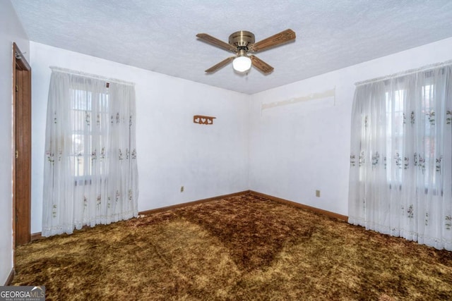 unfurnished room featuring a textured ceiling, carpet flooring, a wealth of natural light, and baseboards