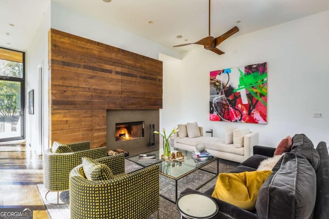 living room featuring a ceiling fan, a lit fireplace, and wood finished floors