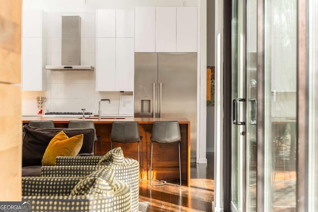 kitchen featuring wall chimney range hood, stainless steel fridge, modern cabinets, and white cabinets