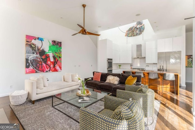 living area with ceiling fan, a towering ceiling, baseboards, and wood finished floors