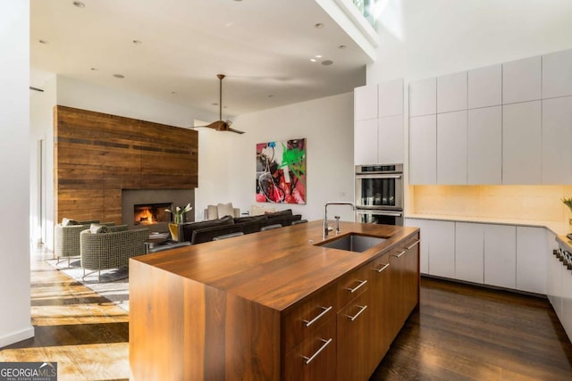 kitchen with modern cabinets, dark wood-type flooring, a lit fireplace, double oven, and a sink