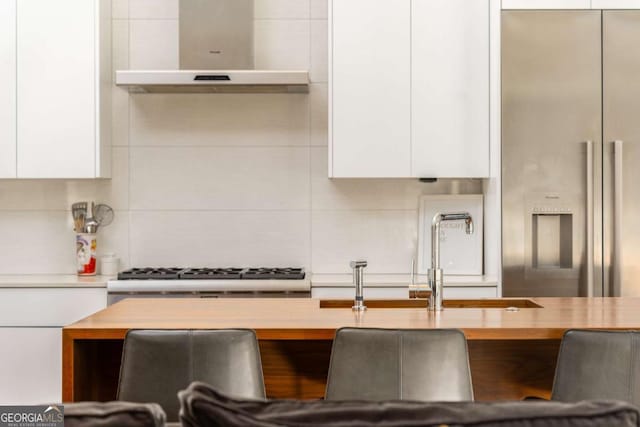 kitchen with wood counters, white cabinetry, backsplash, range hood, and modern cabinets