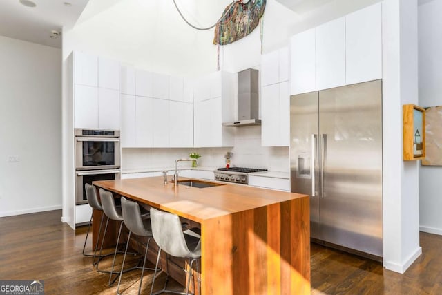 kitchen featuring dark wood-style floors, wall chimney exhaust hood, appliances with stainless steel finishes, and a sink