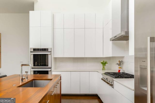 kitchen featuring a sink, wall chimney range hood, appliances with stainless steel finishes, backsplash, and modern cabinets