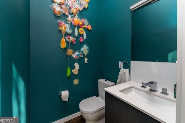 half bathroom featuring baseboards, vanity, and toilet