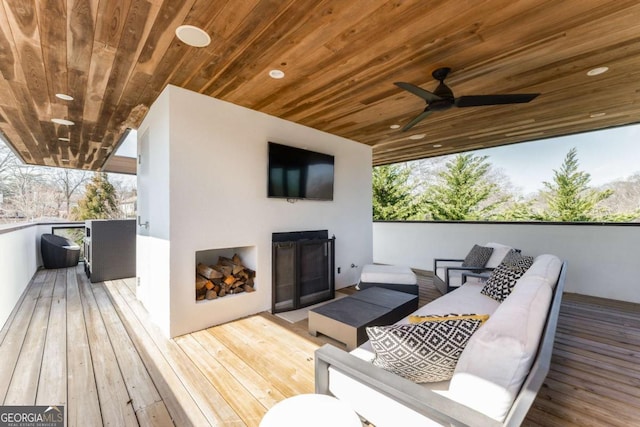 deck with an outdoor living space with a fireplace and a ceiling fan