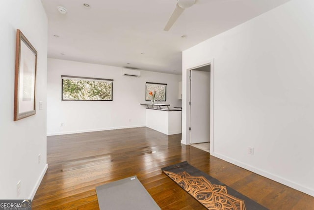 empty room featuring a wall unit AC, baseboards, a ceiling fan, and hardwood / wood-style floors