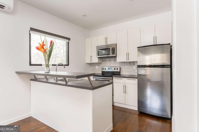 kitchen featuring white cabinets, appliances with stainless steel finishes, backsplash, dark countertops, and dark wood finished floors