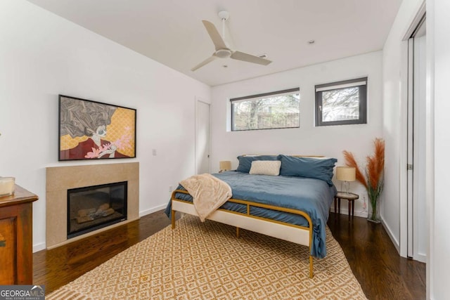 bedroom featuring wood finished floors, a ceiling fan, baseboards, a closet, and a glass covered fireplace