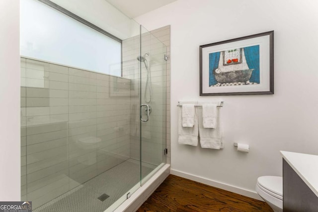 full bathroom featuring toilet, wood finished floors, vanity, baseboards, and a stall shower