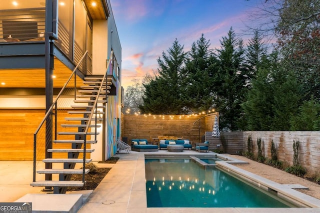 pool at dusk featuring a patio, stairway, fence, a pool with connected hot tub, and outdoor lounge area