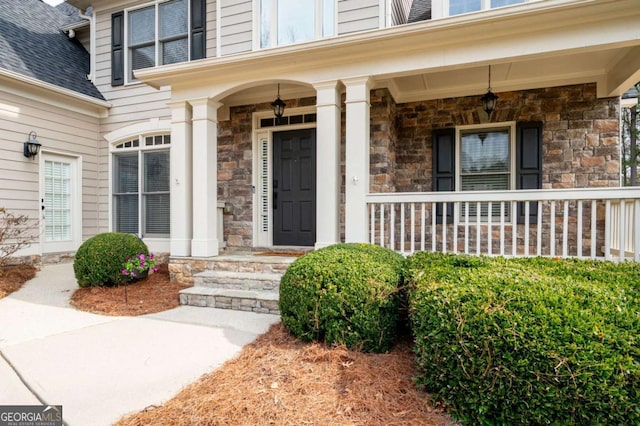 entrance to property featuring a shingled roof, stone siding, and covered porch