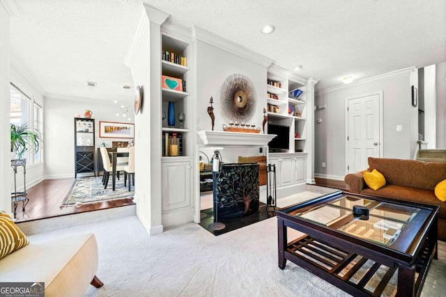 carpeted living area with a textured ceiling, built in shelves, a fireplace, and crown molding