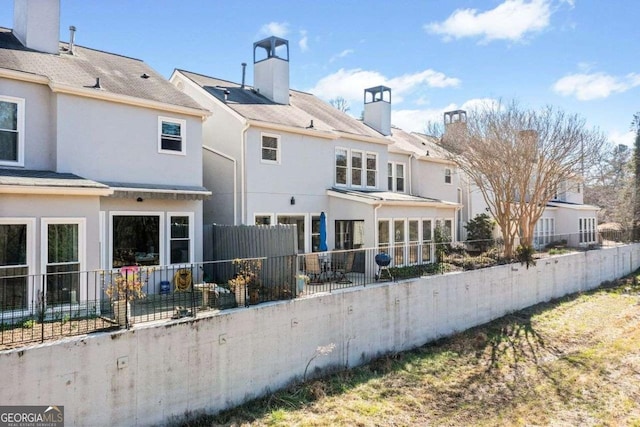 rear view of property with fence private yard, a chimney, and stucco siding