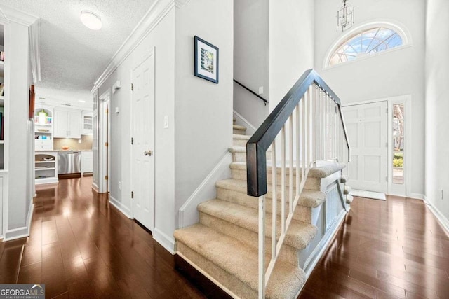 foyer with dark wood-style flooring, ornamental molding, a textured ceiling, baseboards, and stairs