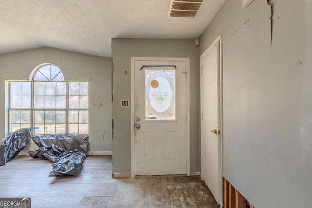 entrance foyer featuring a textured ceiling, vaulted ceiling, wood finished floors, and visible vents