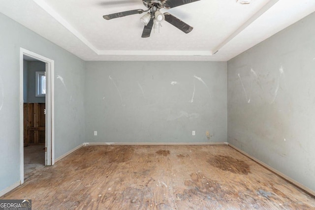 empty room with a tray ceiling, a ceiling fan, and baseboards