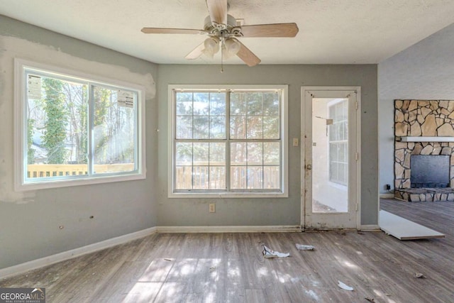 doorway to outside with a ceiling fan, a fireplace, baseboards, and wood finished floors