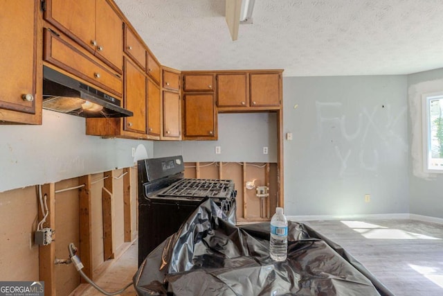 kitchen featuring black gas range, under cabinet range hood, brown cabinetry, and a textured ceiling