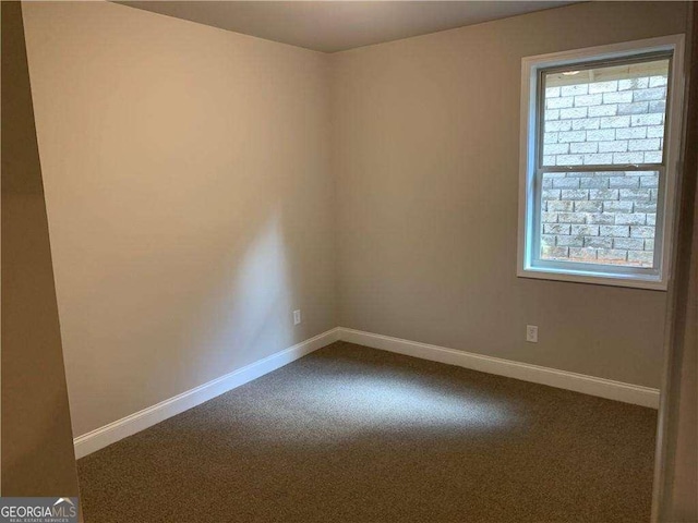 empty room with dark colored carpet, a wealth of natural light, and baseboards