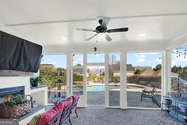 sunroom with a warm lit fireplace, a ceiling fan, and a healthy amount of sunlight