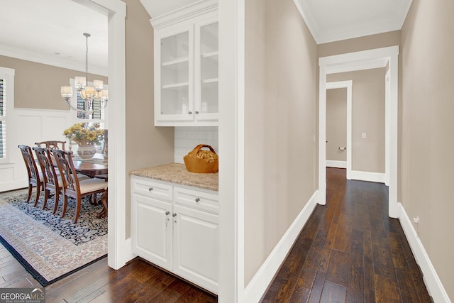 hallway featuring a wainscoted wall, an inviting chandelier, dark wood finished floors, and crown molding