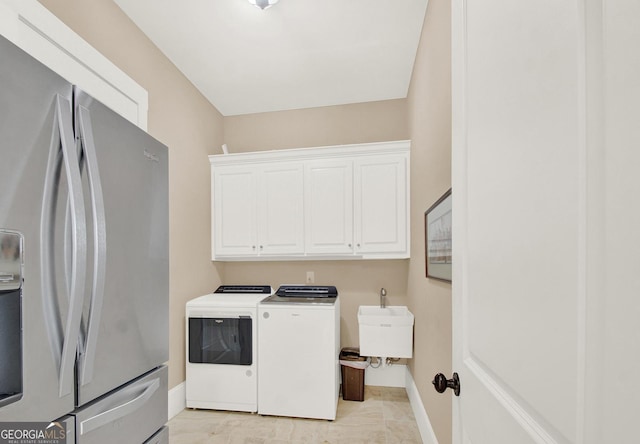 clothes washing area with cabinet space, a sink, washer and clothes dryer, and baseboards