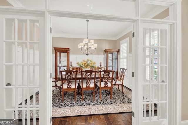 dining space featuring a wainscoted wall, dark wood finished floors, crown molding, a decorative wall, and a chandelier