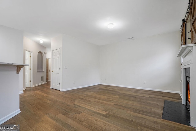 unfurnished living room featuring dark wood-style floors, arched walkways, visible vents, a fireplace with flush hearth, and baseboards