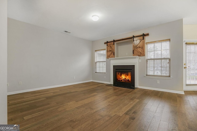 unfurnished living room with a warm lit fireplace, dark wood-type flooring, visible vents, and baseboards