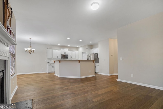 kitchen featuring appliances with stainless steel finishes, a breakfast bar, wood finished floors, a fireplace, and white cabinetry