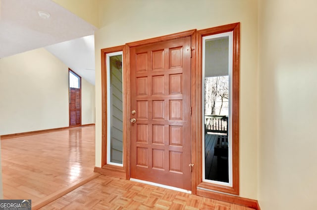 entryway featuring lofted ceiling, parquet flooring, and baseboards