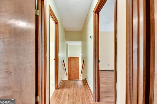 corridor with a textured ceiling, light wood-style flooring, visible vents, an upstairs landing, and baseboards