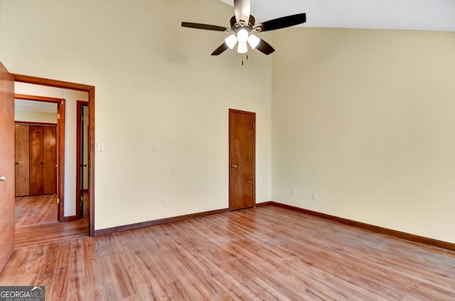 spare room with baseboards, ceiling fan, a towering ceiling, and light wood-style floors