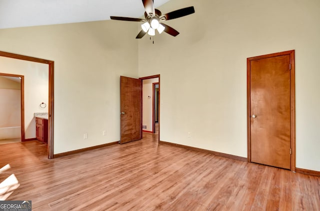 unfurnished bedroom with high vaulted ceiling, ensuite bath, light wood-style flooring, and baseboards