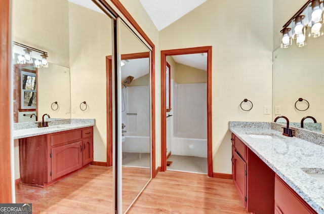 bathroom featuring vaulted ceiling, double vanity, a sink, and wood finished floors