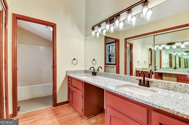 full bathroom with a washtub, double vanity, a sink, and wood finished floors