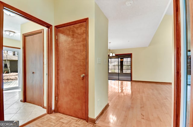 hall with a chandelier, parquet floors, and baseboards