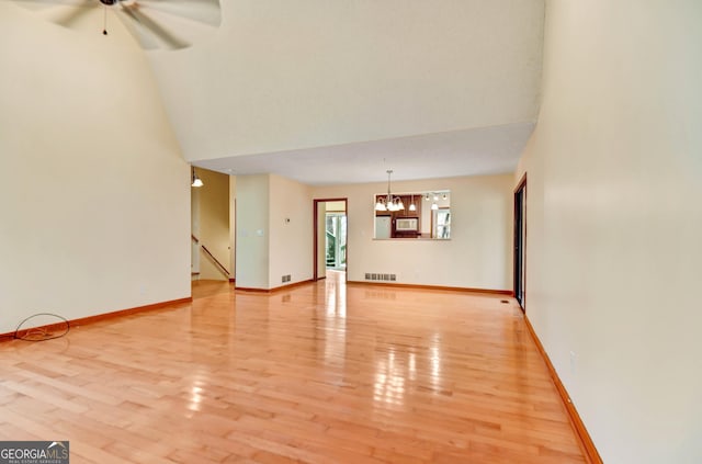 unfurnished living room with light wood finished floors, visible vents, high vaulted ceiling, baseboards, and ceiling fan with notable chandelier