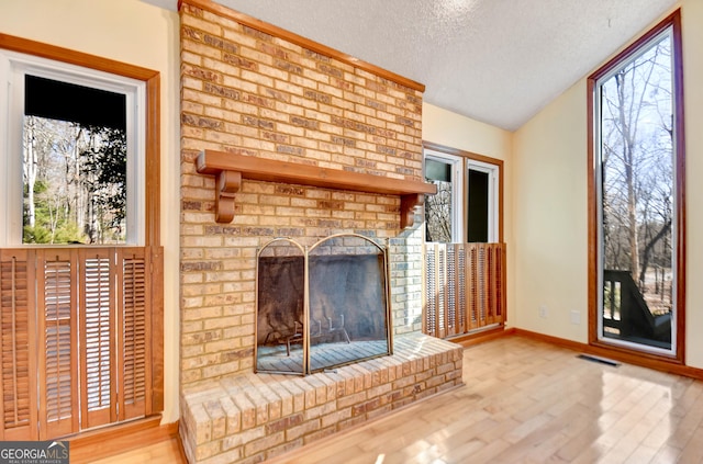 unfurnished living room featuring plenty of natural light, a textured ceiling, visible vents, and wood finished floors