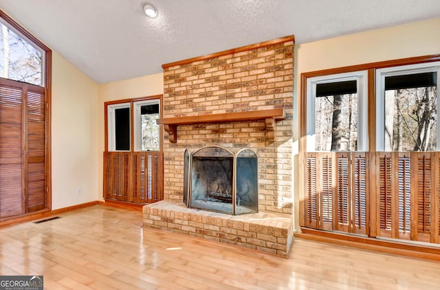 unfurnished living room with a fireplace, lofted ceiling, visible vents, a textured ceiling, and wood finished floors