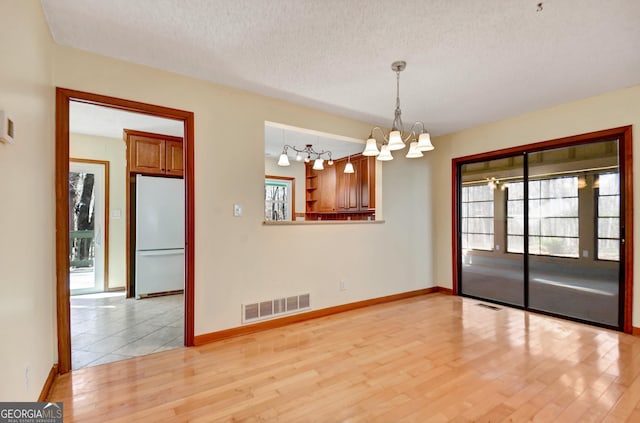 unfurnished room with light wood-style flooring, a healthy amount of sunlight, visible vents, and an inviting chandelier