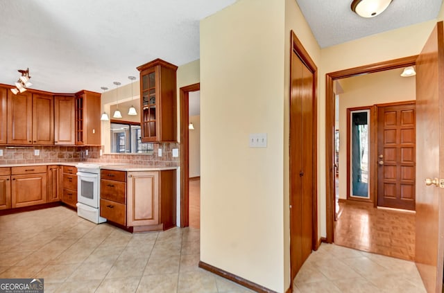 kitchen featuring brown cabinetry, glass insert cabinets, light countertops, white electric range, and backsplash